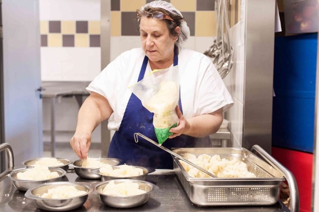Kitchen staff worker seasoning cauliflower for French school lunch.