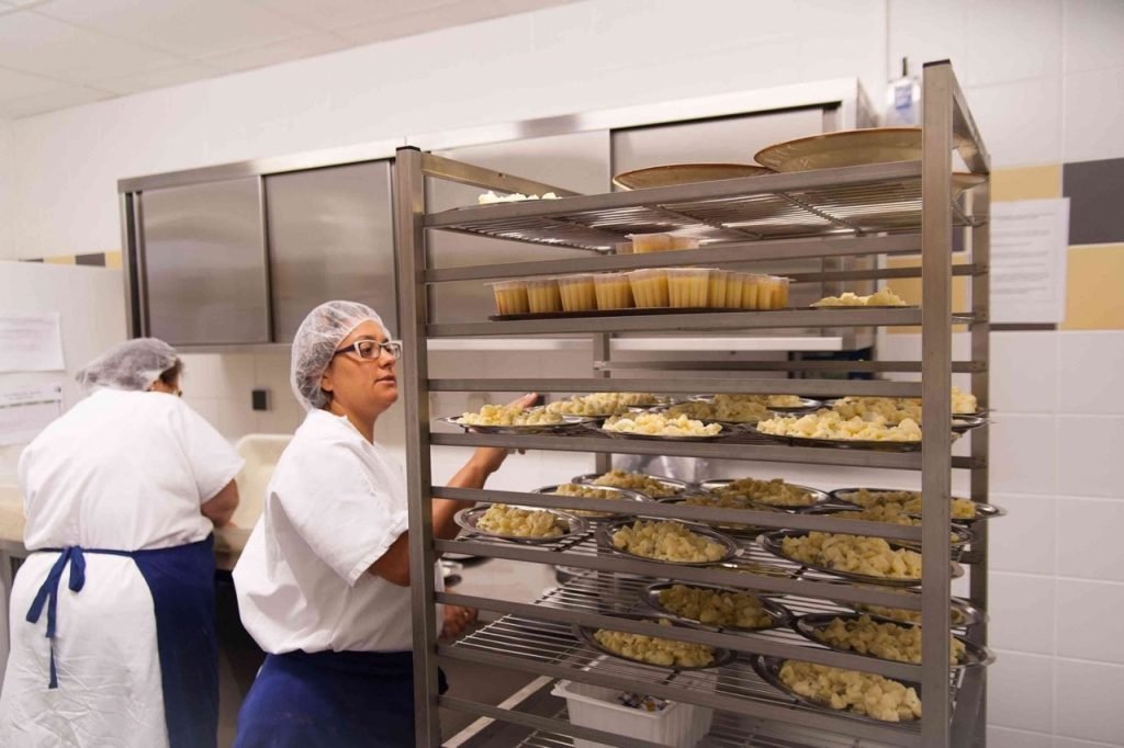 Kitchen staff worker preparing cheese and desserts for French school lunch.