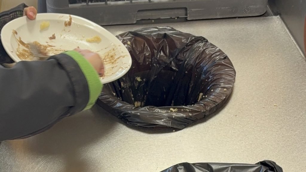 Child scraping leftover food into the bin at the waste-sorting station in a French school cafeteria.