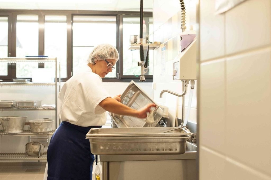 Kitchen staff worker cleaning up trays inside French school cafeteria kitchen.