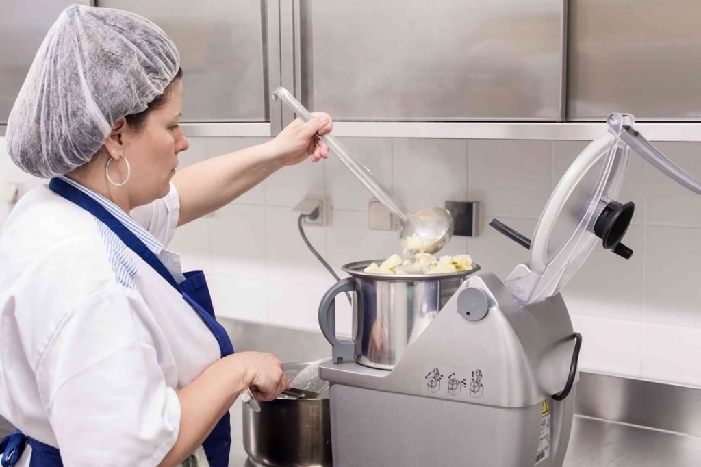 Kitchen staff worker steaming vegetables to make soup for French school lunch.