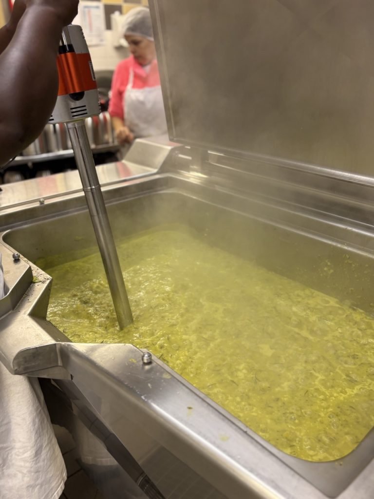 Kitchen staff worker making zucchini soup inside French school cafeteria kitchen.