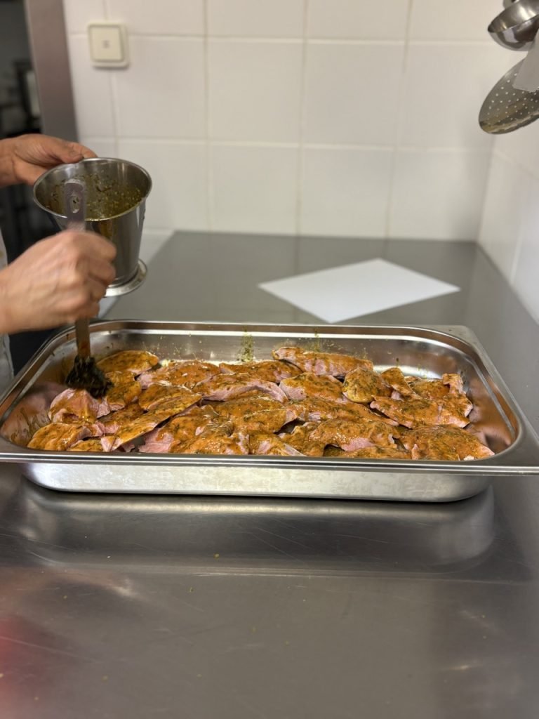 Kitchen staff worker marinating meat inside kitchen of French school cafeteria.