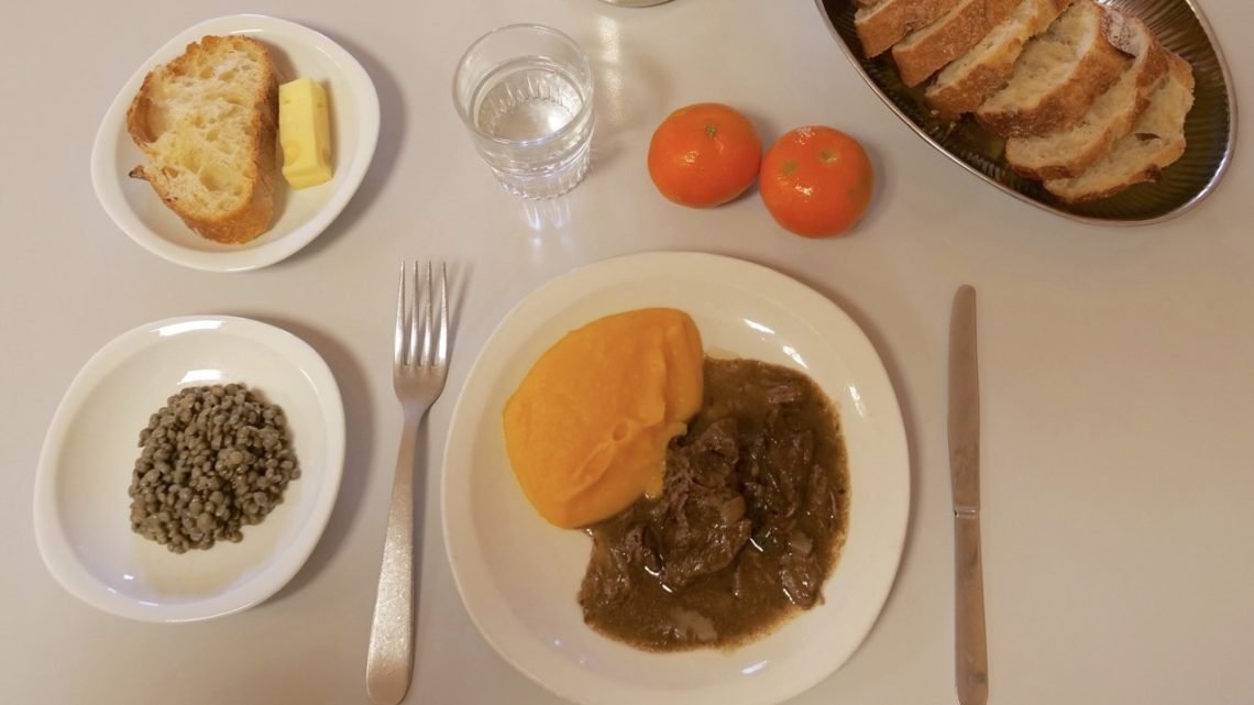 French school lunch tray with beef stew, carrot purée, green lentils, bread, cheese, water, and clementines served in 2022.