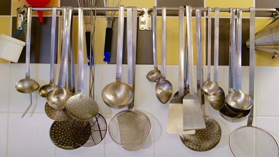 An assortment of hanging utensils on wall of French school cafeteria kitchen.