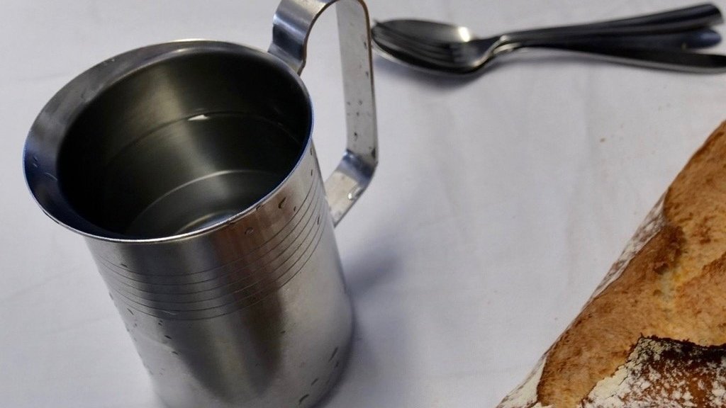 Metal water jug on a table in a French school lunchroom, showing how children drink water with every meal.