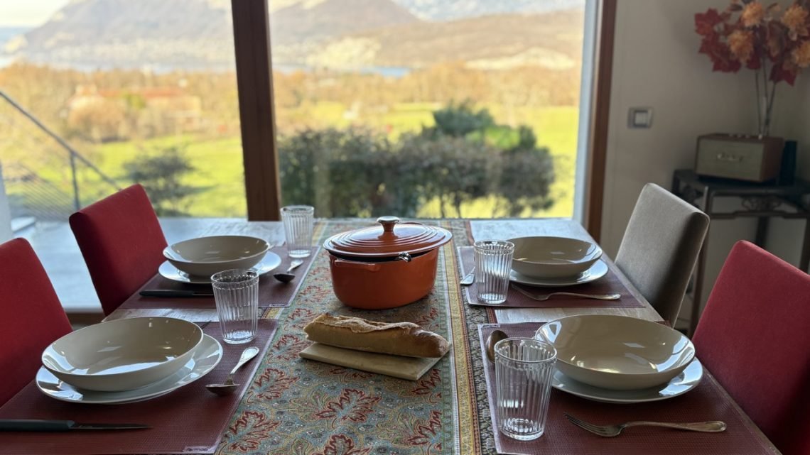 French dining table set for a meal with views of the mountains and Lake Annecy in winter sunlight.