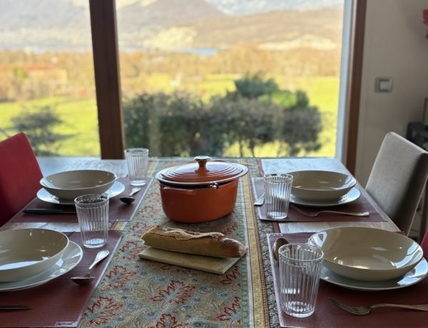 French dining table set for a meal with views of the mountains and Lake Annecy in winter sunlight.